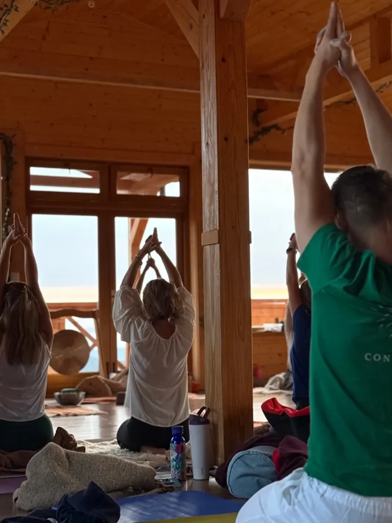 Group practising Kundalini Yoga with arms raised in a wooden hall